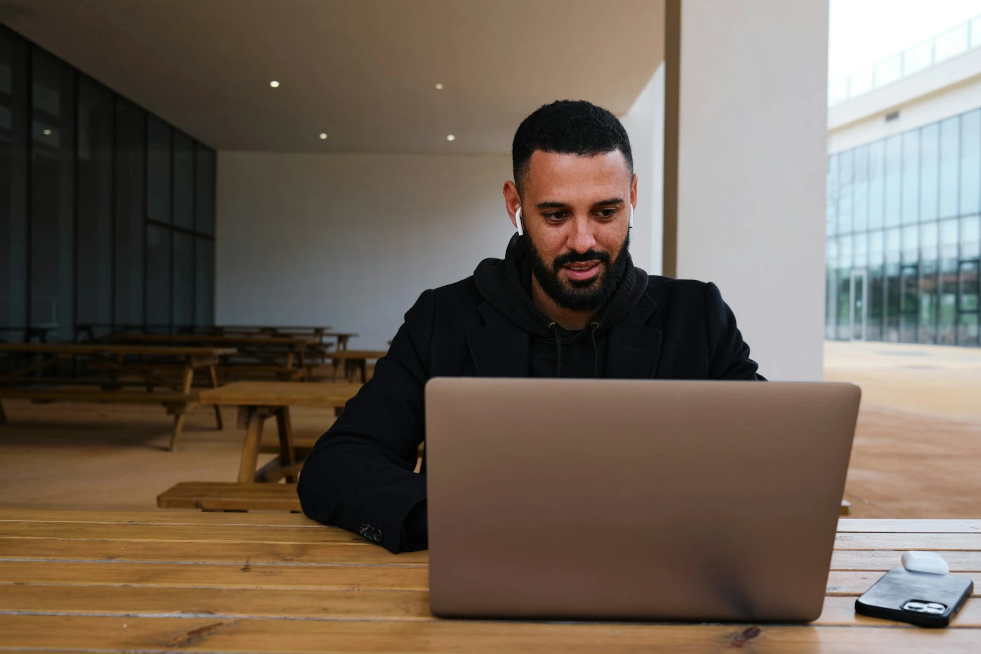 A man wearing wireless earbuds working on a laptop at an outdoor table.